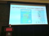 Nicole Siggins stands at a podium, presenting a past MapSwipe use case.